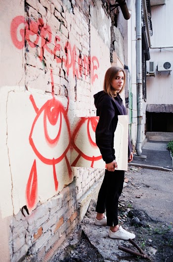 Photo of Woman Wearing a Hoodie and Black Pants Standing Near Wall