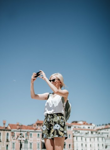 Photo of Woman Wearing Black and White Floral Short and White Tank Top Taking Photo Using Black Smartphone