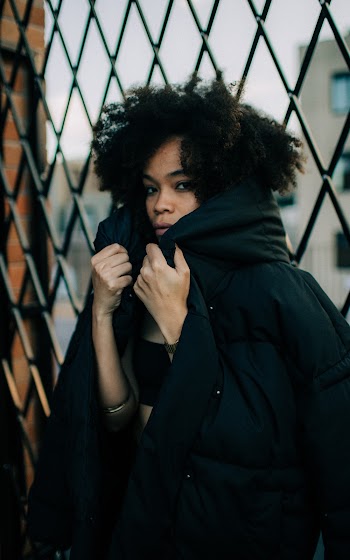 Photo of Woman Wearing Black Hooded Jacket Leaning on Cyclone Fence