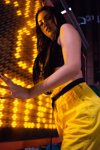 Photo of Woman Wearing Black Sports Bra and Yellow Pants Posing in Front of Yellow Neon Sign