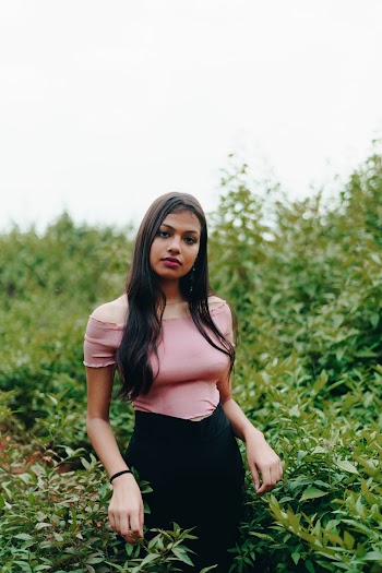 Photo of Woman Wearing Pink Off-shoulder Top and Black Skirt Standing Near Green-leafed Plants