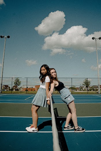 Photo of Woman Wearing White and Blue Dress Standing on Tennis Field With Girl Wearing Black Tank Top and Blue Denim Shorts