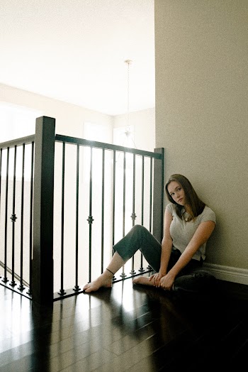 Photo of Woman Wearing White Blouse and Black Pants Sitting on Brown Wooden Plankboard Beside of Stair Rail