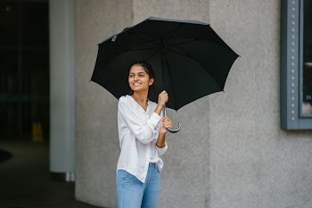 Photo of Woman Wearing White Long-sleeved Shirt and Blue Jeans Holding Black Umbrella