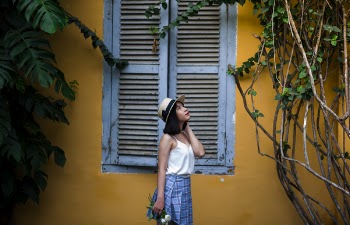 Photo of Woman Wearing White Sleeveless Top and Hat Holding Flowers Near Window