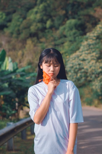 Photo of Woman Wearing White T-Shirt Holding Orange-petaled Flower
