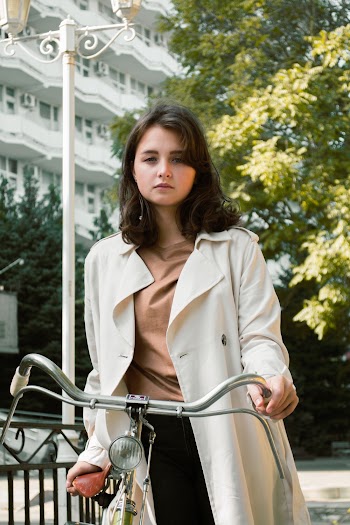 Photo of Woman Wearing White Trench Coat While Holding onto Bicycle