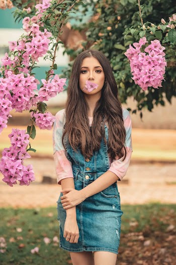Photo of Woman with Pink Flower in Her Mouth Posing Next to Bougainvillea Plant 