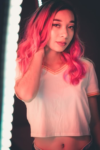 Photo of Woman with Pink Hair Wearing White V-neck Crop-top Holding Her Neck