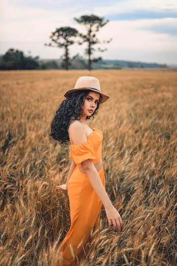 Photo of Women in Orange Outfit and Brown Fedora Standing in Grass Field Posing