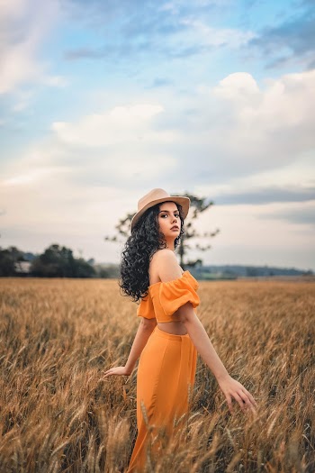 Photo of Women in Orange Outfit and Brown Fedora Standing in Grass Field Posing