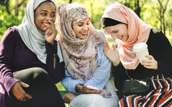 Photo of Women Laughing and Dressed in Hijabs Sitting Next to Each Other.