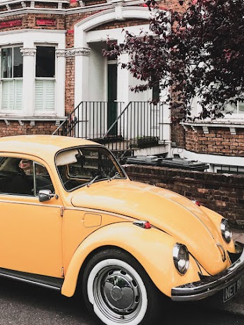 Photo of Yellow VW Beetle Parked by the Curb Next to a House