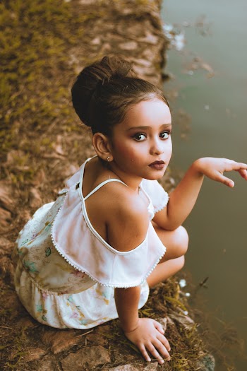 Photo of Young Girl in Make-up Wearing White Off-shoulder Dress Sitting Near Body of Water