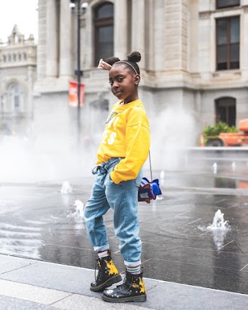 Photo of Young Girl in Yellow Sweatshirt, Blue Jeans and, Black Leather Boots Standing Near Ground Fountain Posing