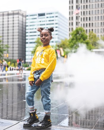 Photo of Young Girl in Yellow Sweatshirt, Blue Jeans and, Black Leather Boots Standing Near Ground Fountain Posing