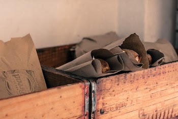 Photograph of Food Packaged  in Grey Kraft Paper Bags Placed  in Brown Wooden Open Boxes