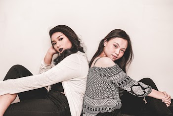 Photograph of two women sitting while leaning on each other back to back