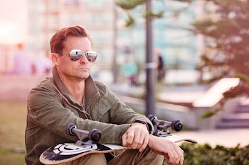 Photography of Man Sitting and Holding White and Black Skateboard