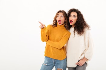 Picture of two shocked girls in sweaters pointing and looking away over white bachground Free Photo