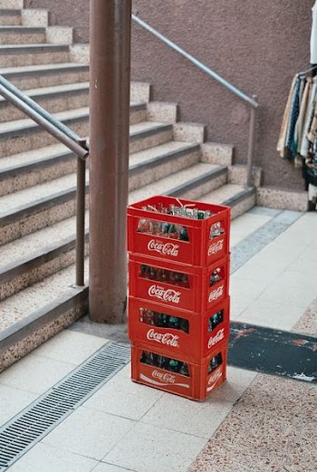 pile of four red Coca-Cola bottle crates near stairs