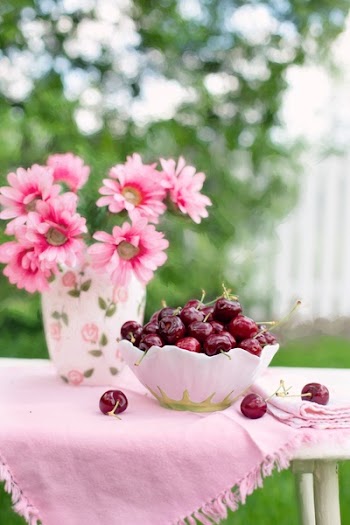 Pink Petaled Flower Beside White and Green Bowl Full of Cherry