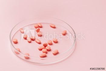 Pink pills on glass plate on pink background