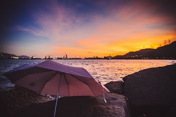 pink umbrella on stone near body of water at golden hour