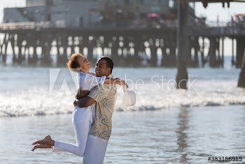 Playful active senior couple hugging on sunny ocean beach