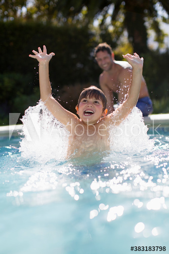 Playful boy splashing in sunny swimming pool