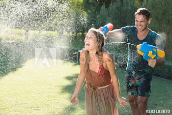 Playful couple with squirt guns in sunny summer backyard