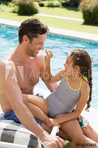 Playful daughter applying sunscreen to nose of father at sunny poolside