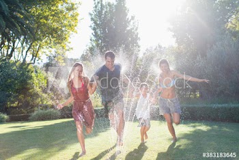Playful family running through sprinkler in sunny summer backyard