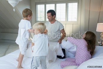 Playful father and kids in pajamas on bed
