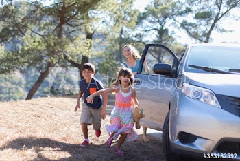 Playful mother and children running outside car at sunny roadside