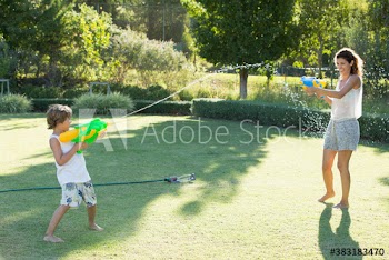 Playful mother and son with squirt guns in sunny summer backyard