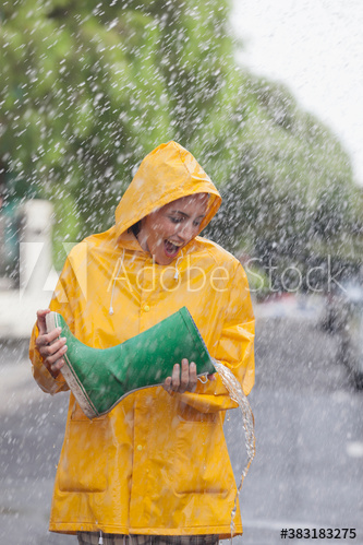 Playful woman empty water from rain boot on rainy street