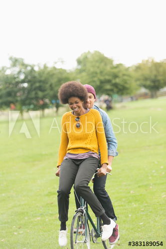 Playful young couple riding bicycle in park grass