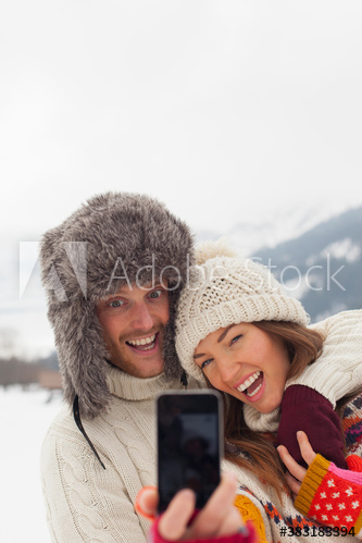 Playful young couple taking selfie in snow