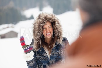 Playful young woman in fur hood with snowball