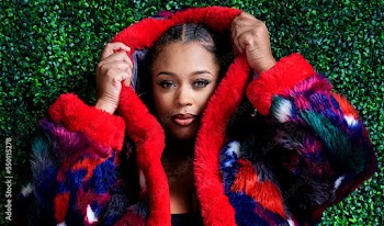 Plus size Black woman sitting in front of grass wall with coat bra and panty on