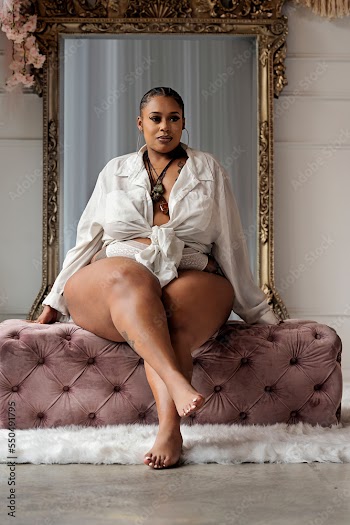 Plus size Black woman sitting on pink bench in front of mirror