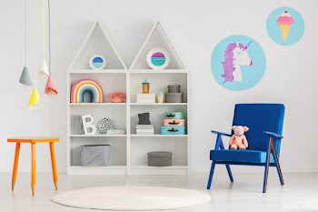 Plush toy on a blue armchair and colorful pendant lamps above an orange table with crayon legs in a cute child bedroom interior
