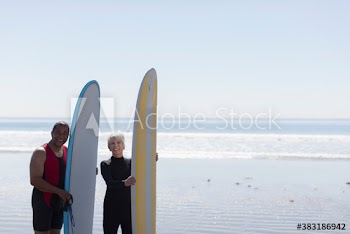 Portrait active senior couple with surfboards on sunny beach