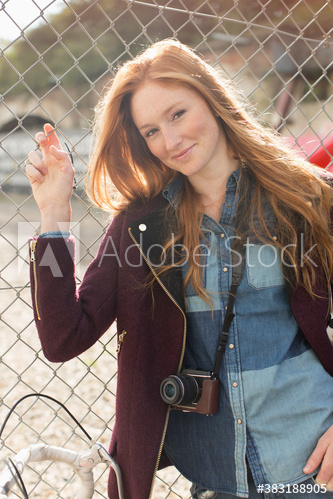 Portrait beautiful young woman with camera at chainlink fence
