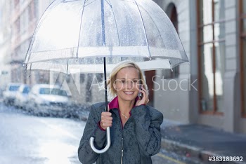 Portrait businesswoman with umbrella talking on smart phone in rain