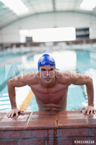 Portrait confident athletic male swimmer at edge of swimming pool