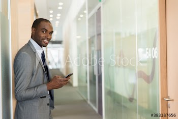Portrait confident businessman using smart phone in office corridor