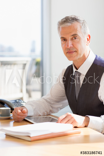 Portrait confident corporate businessman using digital tablet at desk