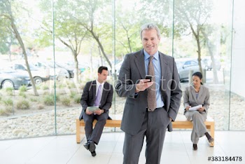 Portrait confident corporate businessman with smart phone in lobby